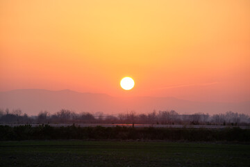 Beautiful evening panoramic landscape with bright setting sun over distant mountain peaks and asphalt road in front at sunset