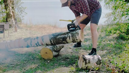 Woodcutter saws off part of a birch from a trunk at a sawmill in the forest
