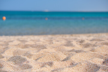 Close up of clean yellow sand surface covering seaside beach with blue sea water on background. Travel and vacations concept