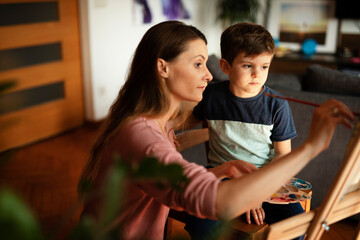 Mother and son painting at home. Little boy drawing with mom in living room..