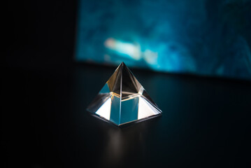 Glowing triangular prism on a table on a black background. Contrast. Prism in the shape of a...