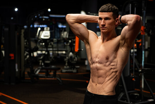 Muscular guy holding arms behind neck flexing six-pack abs in gym, torso