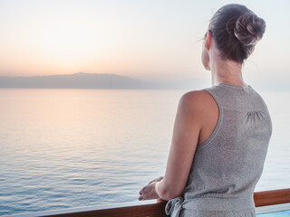 Fototapeta na wymiar Beautiful woman standing on the empty deck of a cruise liner against the backdrop of the setting sun. Closeup, outdoor. Vacation and travel concept