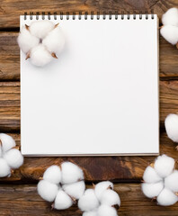 White notepad on brown wood flooring with organic cotton flowers and copy space. natural materials. Blank notepad on a wooden table. Concept.