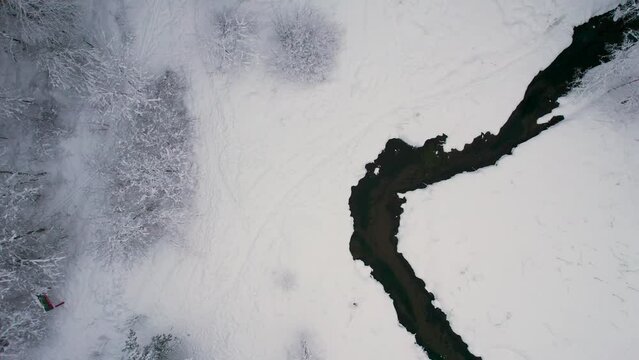 Unfrozen river in winter. Falling snow flakes. Winter coniferous white forest