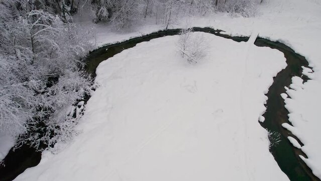 Unfrozen river in winter. Falling snow flakes. Winter coniferous white forest
