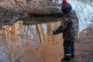 Naklejka premium A little boy in the park in early spring. A child is playing with a homemade fishing rod made of a stick. A carefree childhood.