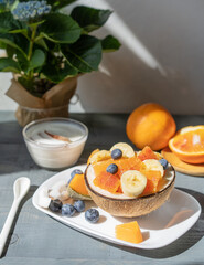Healthy bowl with tropical fruits, cup of caffe, yogurt on grey wooden background