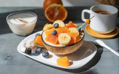 Healthy bowl with tropical fruits, cup of caffe, yogurt on grey wooden background