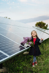 Dreamy girl with a bouquet of flowers on a background of solar panels. Portrait of a smiling child holding lilac flowers in the area near the house. The concept of ecology, a happy future. Happy child