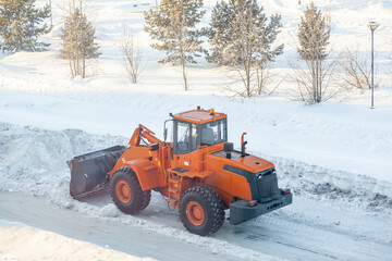 Big orange tractor cleans up snow from the road and loads it into the truck. Cleaning and cleaning...