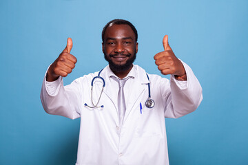 Portrait of cheerful african american doctor giving thumbs up in medical uniform with stethoscope...