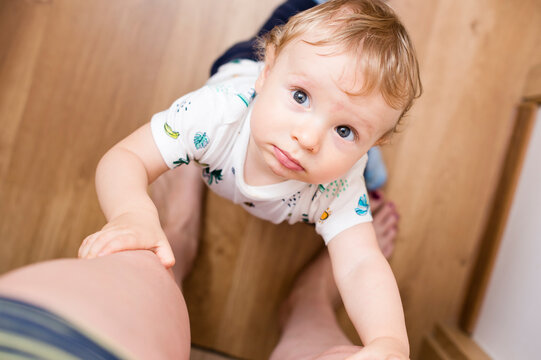 Portrait of a baby boy, embracing mother's leg and asking to talk
