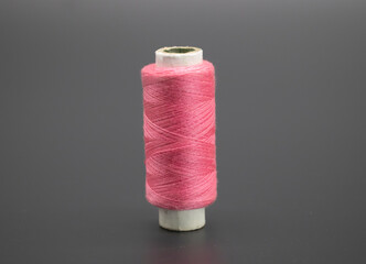 Sewing thread and bobbin in pink color on isolated black background