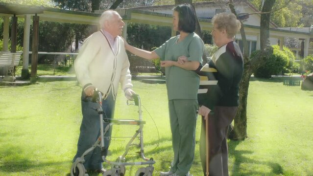 Elderly Man And Woman Speaking To Asian Nurse In The Hospital Garden. Light Rays From Behind