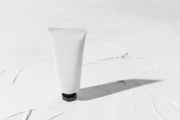 Mockup of blank plastic tube with moisturizer cream, facial cleanser standing on white background with deep shadows. Concept bio organic beauty products