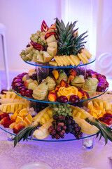 Delicious fruits appetizers, desserts on stand, modern sweet table at wedding or baby shower. Luxury catering concept. Fruit bar at wedding reception, pineapple, apple, orange,grapes