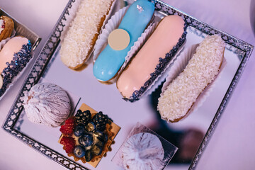 Eclairs set. Amazing fresh colorful homemade eclairs close-up on a tray. Delicious sweets, French eclairs with glaze, cream, decorative elements from fresh berries.