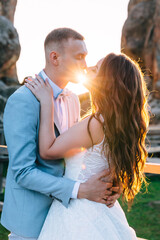 Wedding couple kissing and hugging on rocks at sunset