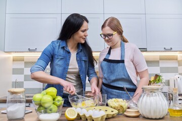 Mother and teenage daughter cooking at home in the kitchen.