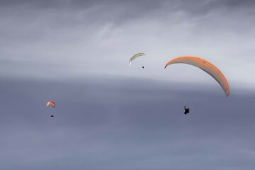 3 people paragliding in a cloudy sky.
