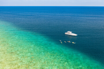 Aerial view or top view of luxury speed boat floating on the crystal clear water at beach. Maldives island adventure aerial landscape, seascape with edge of coral reef, people snorkeling adventure