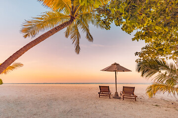Sunset beach. Beautiful tropical island shore, two sun beds lounger, parasol under palm tree. Sand...