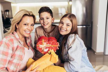 Happy mother's day! Daughter and son congratulates mom and gives her flowers and present.