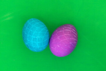 Osterei t&uuml;rkis und lila mit Netzmuster vor gr&uuml;nem Hintergrund