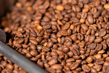 Production of freshly roasted coffee beans. Roasting process in an industrial coffee roasting machine in a factory. Mixing roasted coffee beans. Food and drink background for cafe.