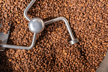 Production of freshly roasted coffee beans. Industrial mixing machine for mixes roasted coffee beans in roaster, close up. Roasting process. Food and drink background for cafe.