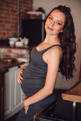 a beautiful pregnant woman in a gray dress in the kitchen in the loft style.