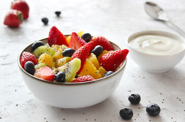 Fruit salad made with strawberry, kiwi and orange, decorated with blueberry and chia seed, served with natural yogurt.