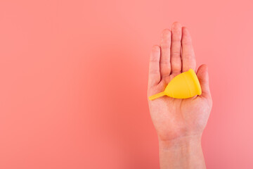 Close up view of woman holding yellow menstrual cup isolated over pink background, woman's period, menstrual cup in hands, modern methods for crytical days. Gynecology and hygiene products concept