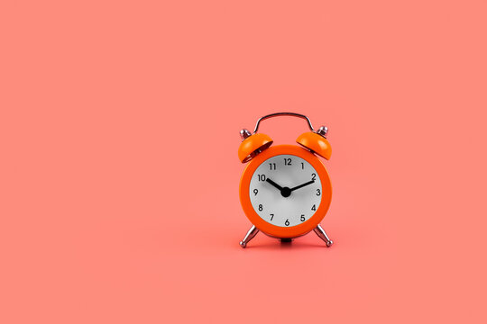 Top view photo of classic little orange alarm clock isolated over light color pastel pink backdrop.