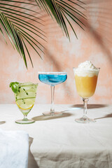 Summer cocktails on a white table over a pink wall in sunlight with the shadow of a palm leaf.