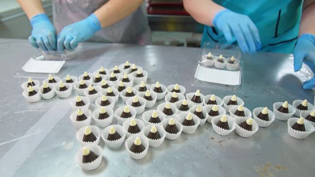 Beautiful delicious candy cones in individual wrapper are on the table. Workers in gloves put sweets into plastic boxes.
