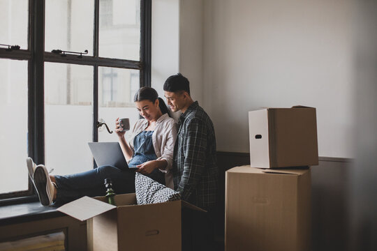 Mid adult couple moving house and using a laptop - Powered by Adobe