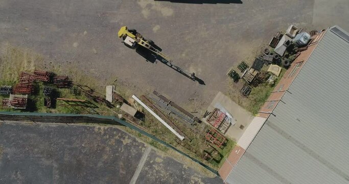 Aerial perspective of a old yellow crane moving a heavy metal bar with help from factory worker moving the product specifically into place.