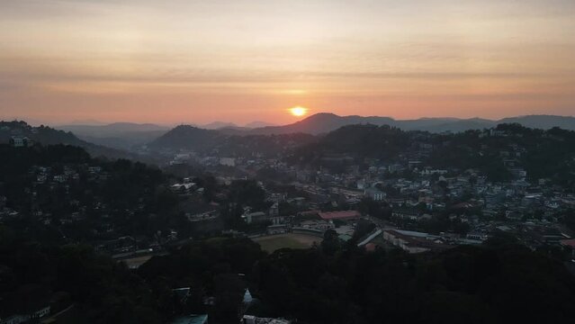 Beautiful sunset between the veil of clouds behind the silhouettes of the hilly landscape of Sri Lanka above the village of Kandy. High angle drone panning tilt shot