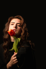 Studio portrait of a young woman in sunglasses, on a black background, with a bouquet of red tulips in her hands. International Women's Day. Valentine's Day.