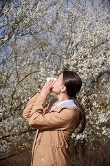 Woman allergic suffering from seasonal allergy at spring, posing in blossoming garden at...