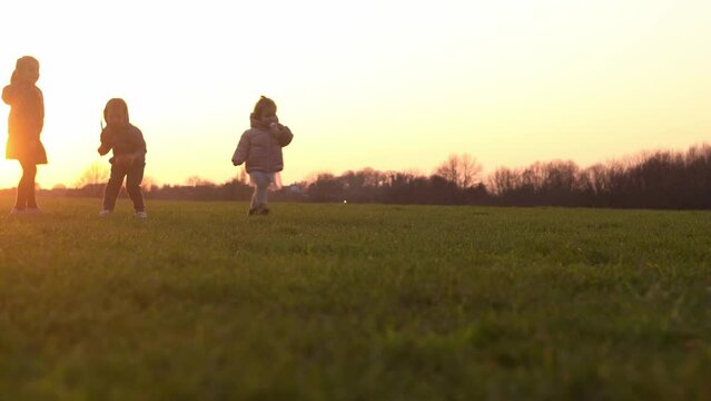 Happy family at sunset. Silhouette of group of people walk in park. child with parents holding hand. Father playing football game on grass. Young Dad fave fun do sport with children siblings outside