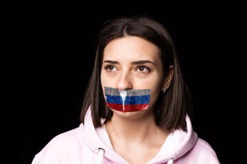 Front camera view. Portrait of young upset girl with three colors duct tape over her mouth isolated on dark background. Censorship, freedom of speech concept.