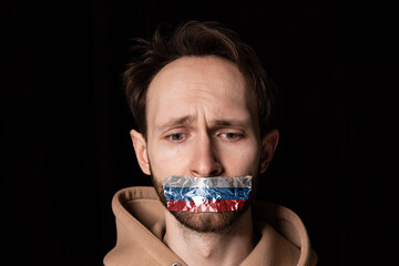 Close-up portrait of young emotive man with three colors duct tape over his mouth isolated on dark...