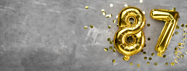 Yellow foil balloon number, number eighty-seven on a concrete background. Greeting card with the inscription 87. Anniversary concept. for anniversary, birthday, new year celebration. banner,