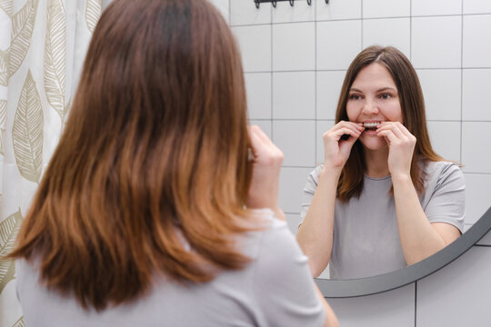 A woman in front of a mirror in the bathroom putting on invisible plastic teeth aligners or braces. Beautiful and healthy smile. Teeth whitening.