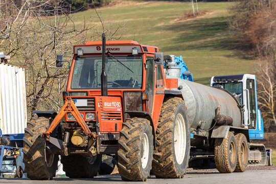 Grafenau, Bavaria, Germany - 2022, March 20th: Portrait of a Fiatagri New Holland 110 90 tractor with a slurry spreader. A takeuchi excavator is seen in the background. Rural farm scenery