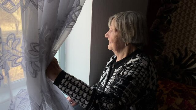 An old woman looks out the window of a rural house in Ternopil region, Ukraine