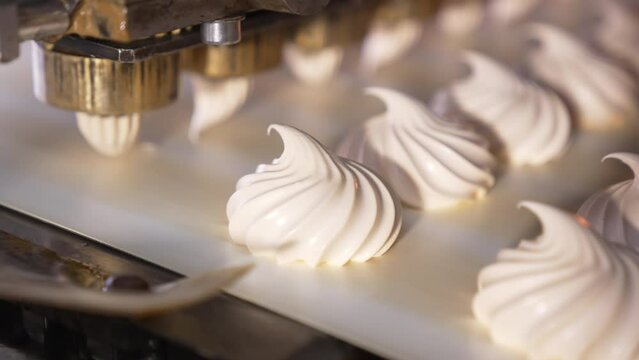 White creamy marshmallows are squeezed on the moving conveyor belt. Close up. Automated line for sweet products manufacturing. Confectionery concept.